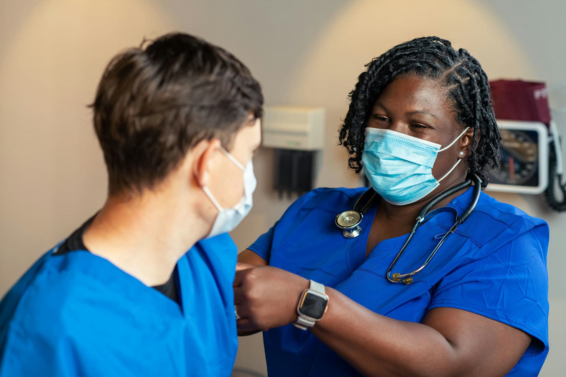 Deux soignants en tenue médicale, l'une ajustant la manche de l'autre